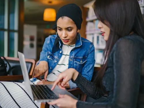 Women at dining table point at laptop